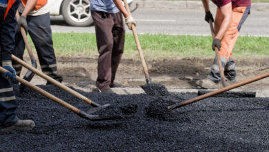 Close view of workers raking and shoveling new blacktop by the curb; team effort in street repair and urban improvement.